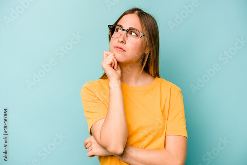 Young caucasian woman isolated on blue background thinking and looking up, being reflective, contemplating, having a fantasy.