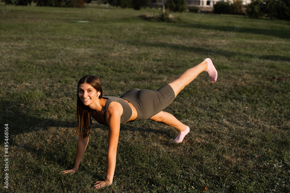 Fototapeta premium Fit girl does warm-up and stretching exercises in green park. Sports lifestyle.