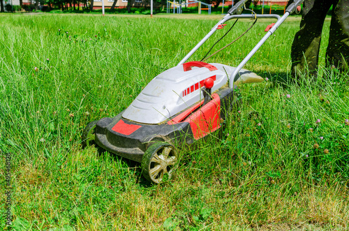 A man mows the grass with an electric lawn mower. Freshly mown grass.