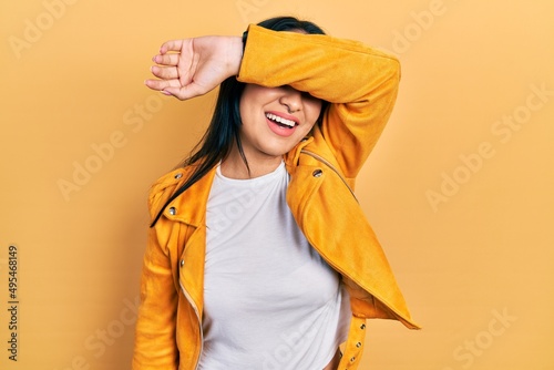 Beautiful hispanic woman with nose piercing wearing yellow leather jacket covering eyes with arm smiling cheerful and funny. blind concept. © Krakenimages.com