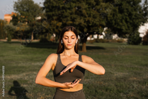 Asian girl does qigong meditation in the green park. Young woman stand in special stance and do special hand movement.