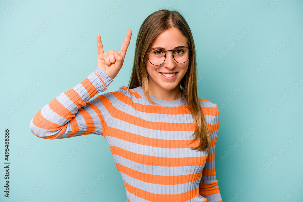 Young caucasian woman isolated on blue background showing a horns gesture as a revolution concept. Young caucasian woman isolated on blue background showing a horns gesture as a revolution concept.