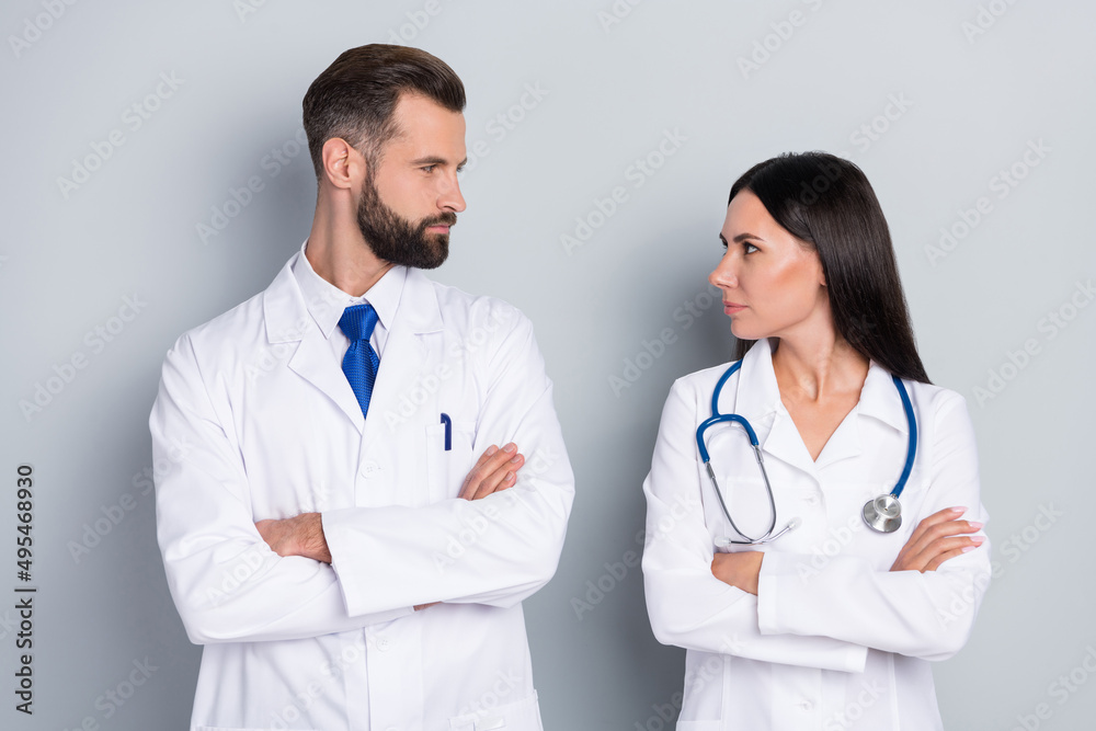 Photo of smart clever two docs dressed white uniform sarms folded looking each other isolated grey color background Photo of smart clever two docs dressed white uniform sarms folded looking each other isolated grey color background