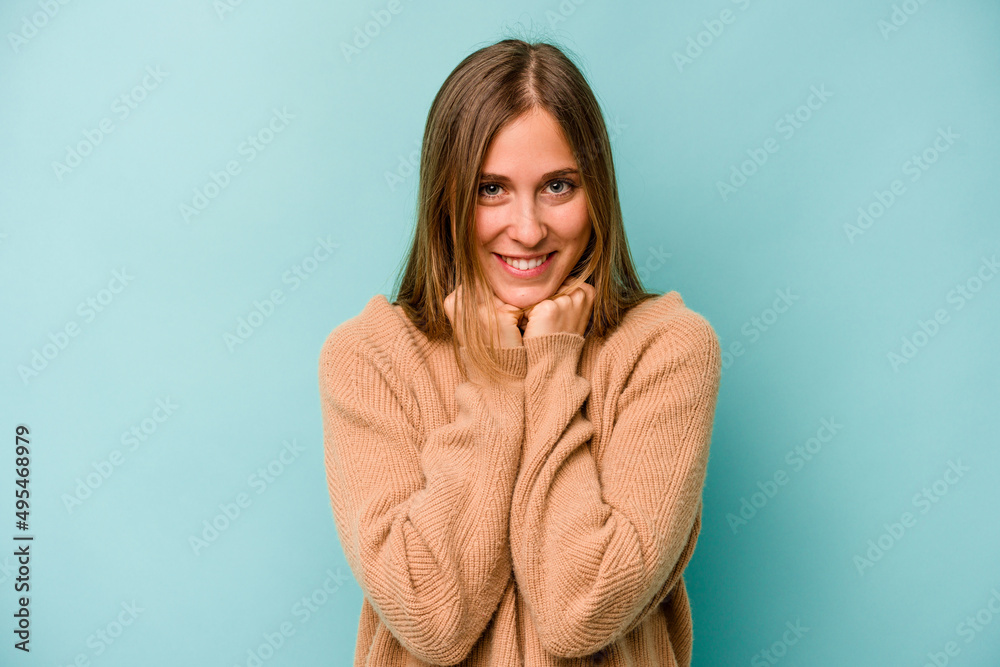Young caucasian woman isolated on blue background keeps hands under chin, is looking happily aside. Young caucasian woman isolated on blue background keeps hands under chin, is looking happily aside.