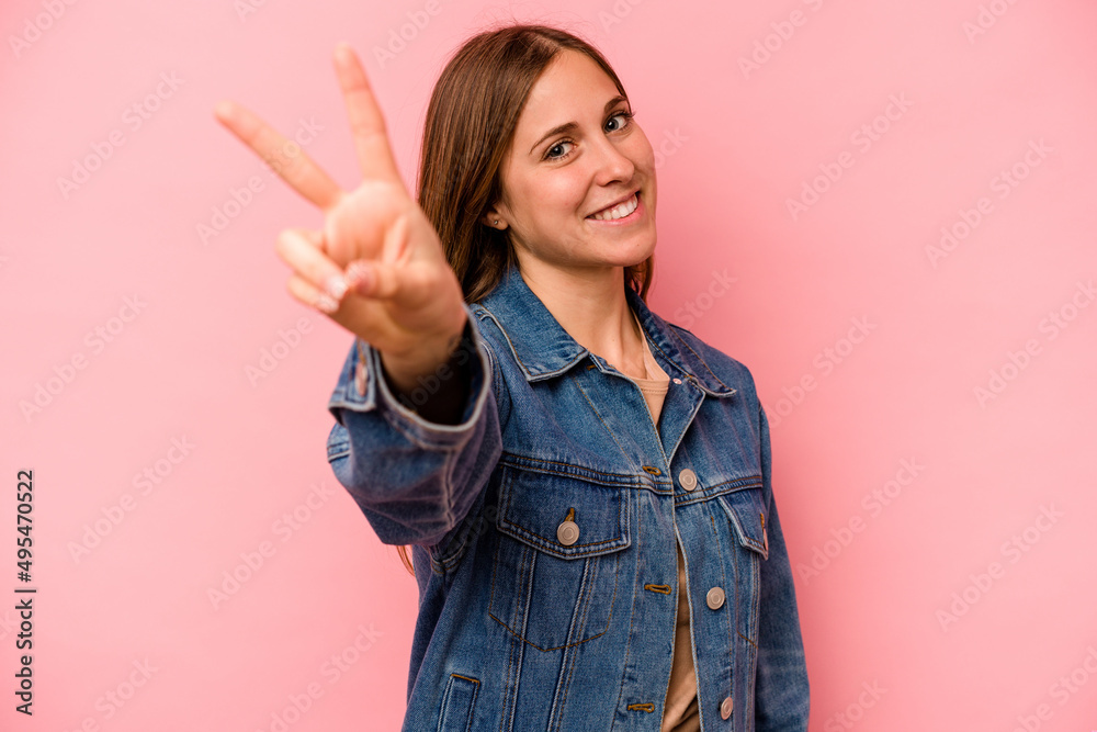 Young caucasian woman isolated on pink background joyful and carefree showing a peace symbol with fingers. Young caucasian woman isolated on pink background joyful and carefree showing a peace symbol with fingers.