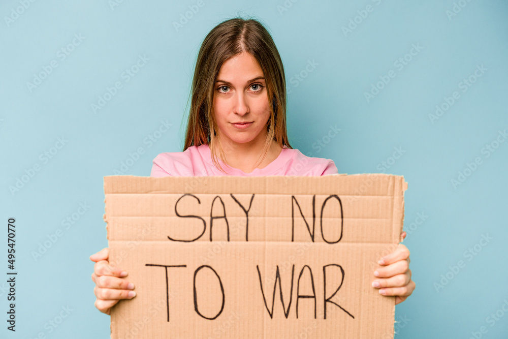 Young caucasian woman holding no war placard isolated on blue background Young caucasian woman holding no war placard isolated on blue background