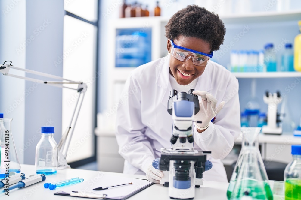 African american woman wearing scientist uniform using microscope at laboratory African american woman wearing scientist uniform using microscope at laboratory