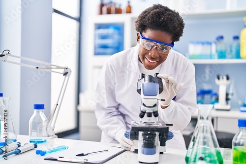 African american woman wearing scientist uniform using microscope at laboratory