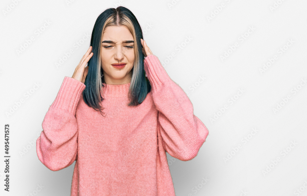 Young modern girl wearing pink wool winter sweater covering ears with fingers with annoyed expression for the noise of loud music. deaf concept.