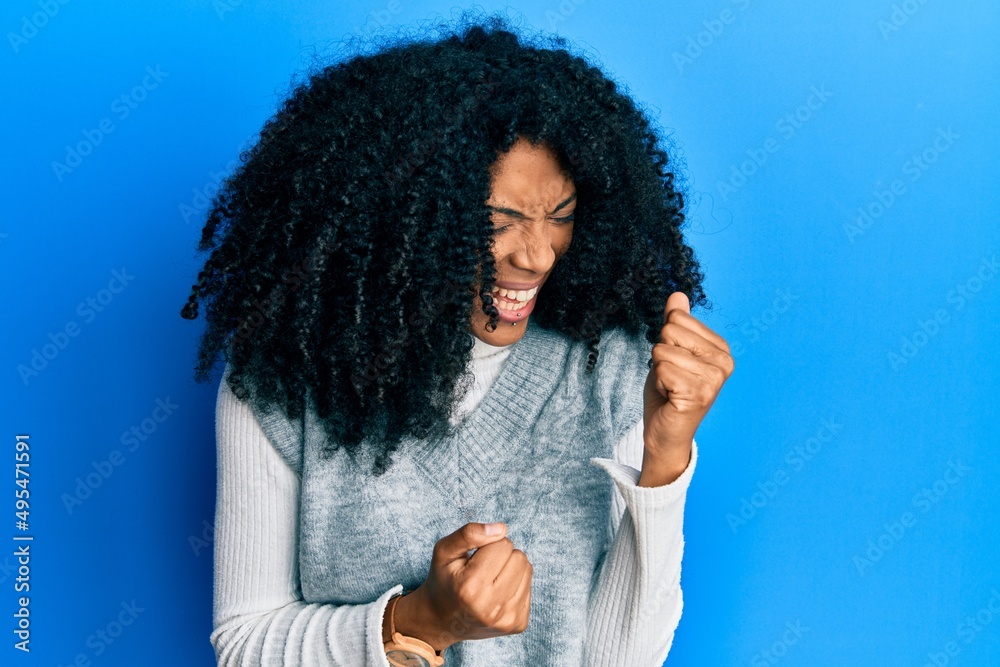 African american woman with afro hair wearing casual winter sweater celebrating surprised and amazed for success with arms raised and eyes closed. winner concept.