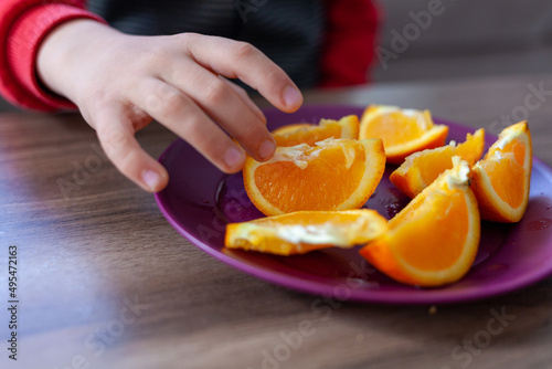Tableau sur toile the boy is holding a slice of orange. A plate of sliced orange.