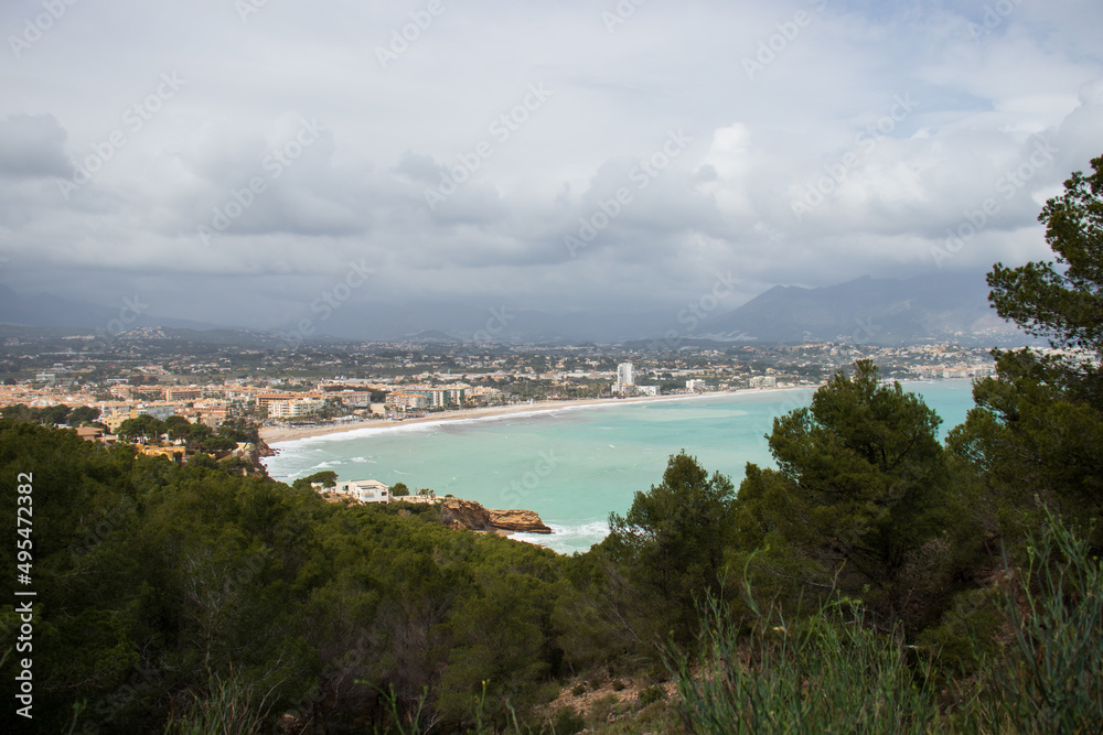 Detail of the coastline of Albir, in the municipality of Alfaz del Pi, with tall buildings next to the beach. Cloudy day and turquoise Mediterranean sea with waves.