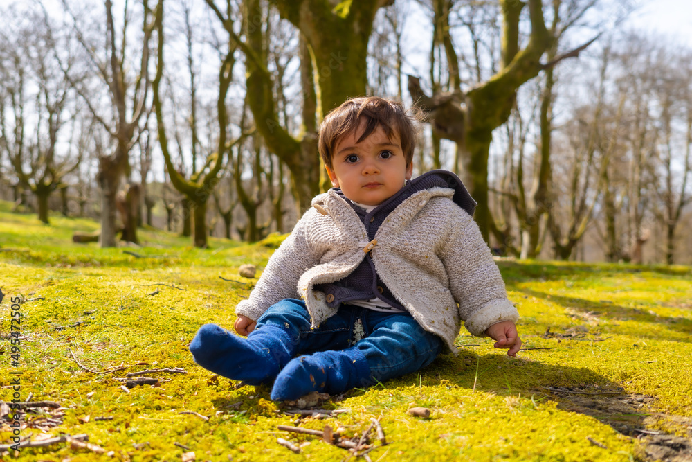 One year old boy sitting forest one spring morning, looking at camera