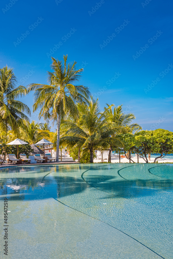 Outdoor tourism landscape. Luxury beach resort with swimming pool and beach chairs or loungers under umbrellas with palm trees and blue sky. Summer travel tourism poolside, beachfront vacation holiday