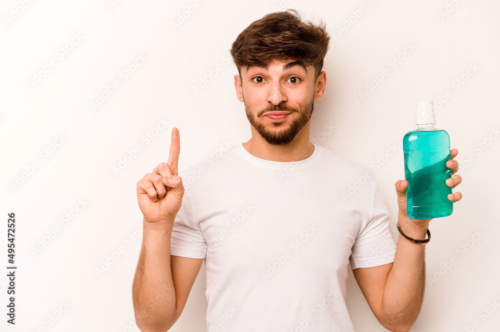 Young hispanic man holding mouthwash isolated on white background showing number one with finger. Young hispanic man holding mouthwash isolated on white background showing number one with finger.