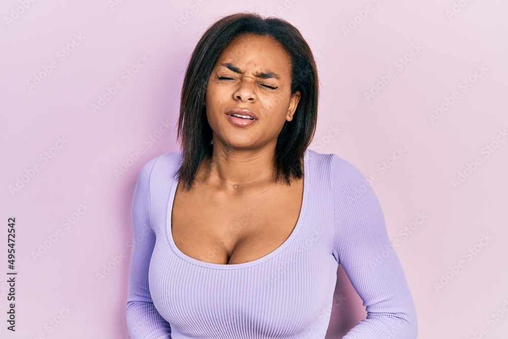 Young african american girl wearing casual clothes with hand on stomach because nausea, painful disease feeling unwell. ache concept. Young african american girl wearing casual clothes with hand on stomach because nausea, painful disease feeling unwell. ache concept.