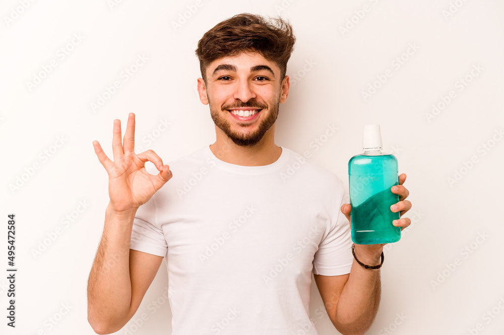 Young hispanic man holding mouthwash isolated on white background cheerful and confident showing ok gesture. Young hispanic man holding mouthwash isolated on white background cheerful and confident showing ok gesture.