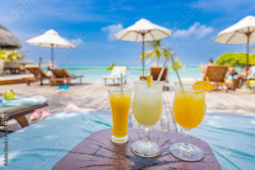 Fototapeta Naklejka Na Ścianę i Meble -  Colorful cocktails on luxury beach resort. Blurred poolside, chairs, beds under umbrella and palm tree leaves. Tropical island beachfront, infinity pool, summer vibes, cool drink glasses