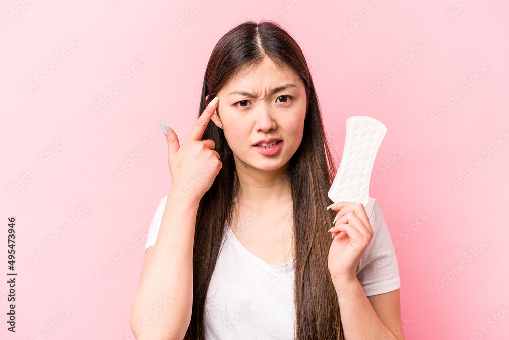 Young asian woman holding sanitary napkin isolated on pink background showing a disappointment gesture with forefinger. Young asian woman holding sanitary napkin isolated on pink background showing a disappointment gesture with forefinger.