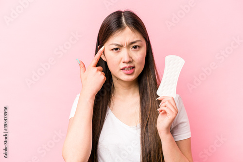 Young asian woman holding sanitary napkin isolated on pink background showing a disappointment gesture with forefinger.