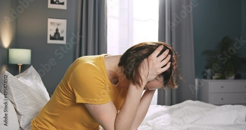 Depressed young caucasian woman sit alone on bed, feel stress anxiety after bad sleep. Beautiful caucasian female waking up in the morning because of seing nightmare. photo