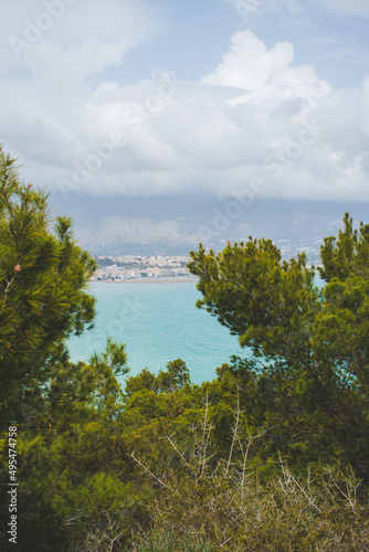 Landscape of the coast of Alicante between pine trees of an intense green color on a cloudy day. Surroundings of the Costa Blanca, with the sea and the town of Albir and Alfaz del Pi on the horizon.