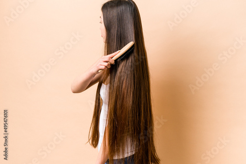 Young asian woman combing her hair isolated on beige background