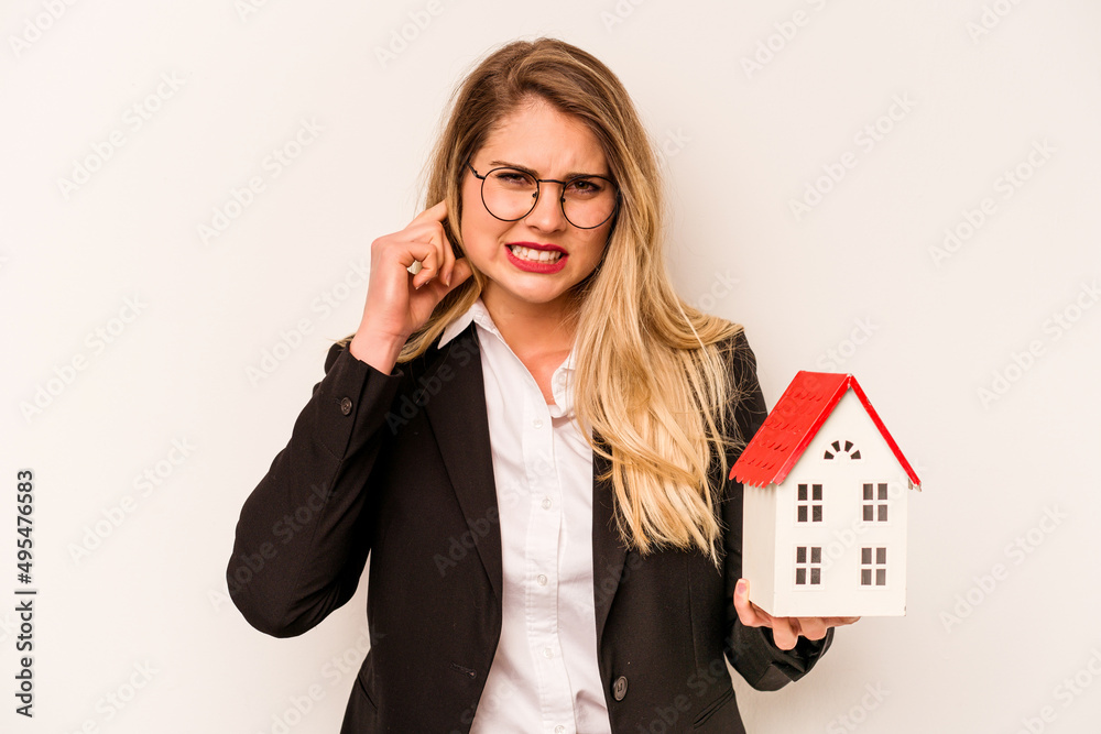 Young business caucasian woman holding a toy house isolated on white background covering ears with hands. Young business caucasian woman holding a toy house isolated on white background covering ears with hands.