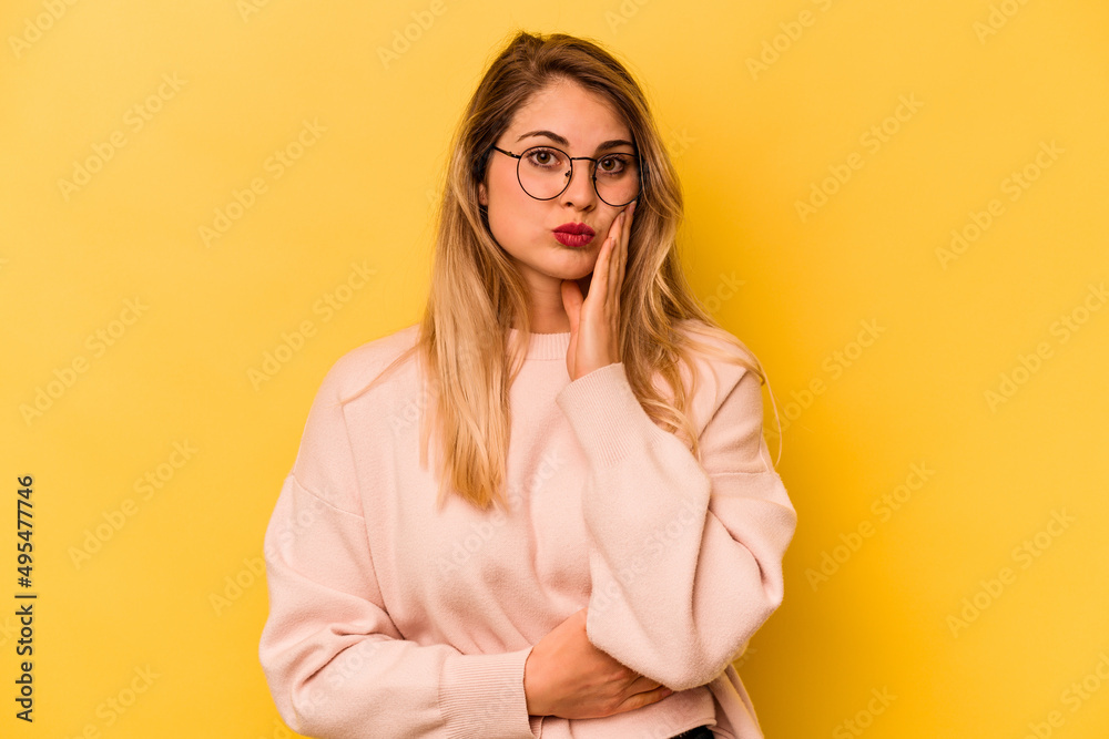 Young caucasian woman isolated on yellow background blows cheeks, has tired expression. Facial expression concept. Young caucasian woman isolated on yellow background blows cheeks, has tired expression. Facial expression concept.