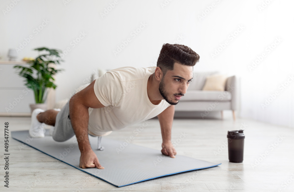Strength workout concept. Fit young Arab man doing push ups or plank at home, full length