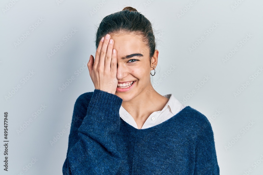 Young caucasian girl wearing casual clothes covering one eye with hand, confident smile on face and surprise emotion. Young caucasian girl wearing casual clothes covering one eye with hand, confident smile on face and surprise emotion.