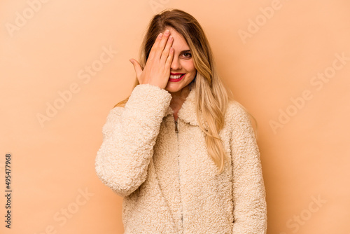 Young caucasian woman isolated on beige background having fun covering half of face with palm.