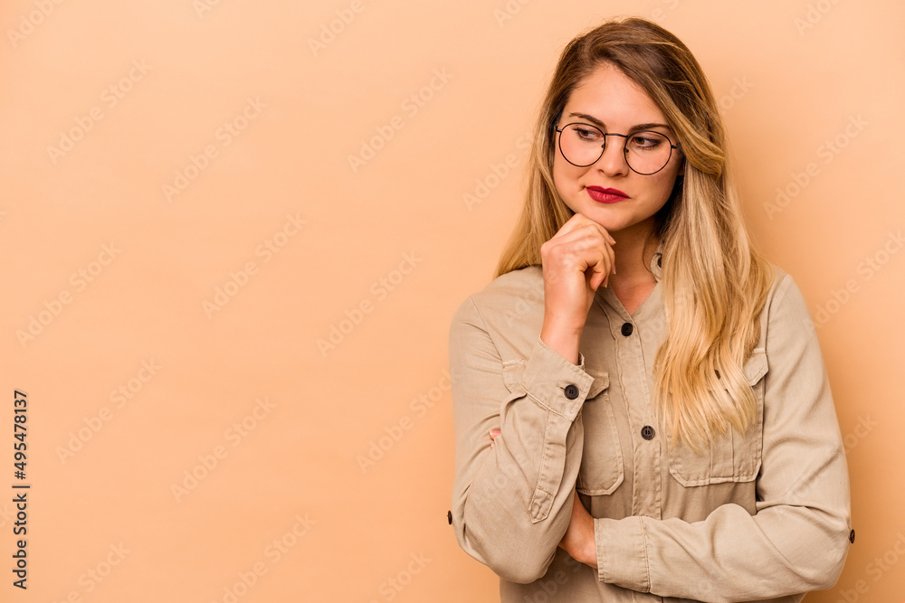 Young caucasian woman isolated on beige background looking sideways with doubtful and skeptical expression. Young caucasian woman isolated on beige background looking sideways with doubtful and skeptical expression.