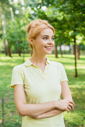 pretty and happy woman standing with crossed arms in park.