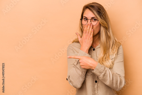 Young caucasian woman isolated on beige background pointing to the side