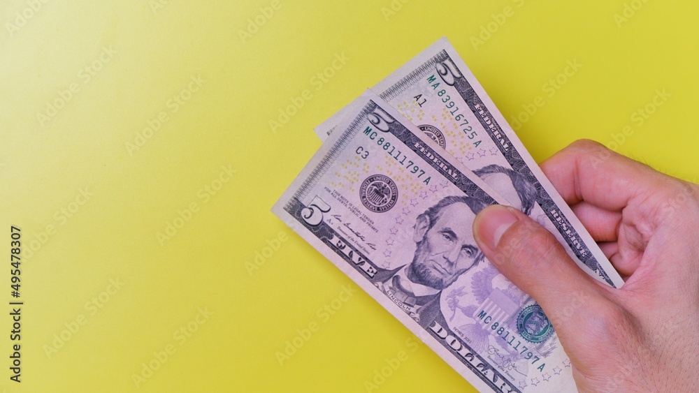 Man's hand is making a payment. Business Investment Economy Money Loan Saving Income Prosperity and Finance concept. Male hand showing dollar bills on yellow background. FIve Dollar. 5 US Dollar. Man's hand is making a payment. Business Investment Economy Money Loan Saving Income Prosperity and Finance concept. Male hand showing dollar bills on yellow background. FIve Dollar. 5 US Dollar.