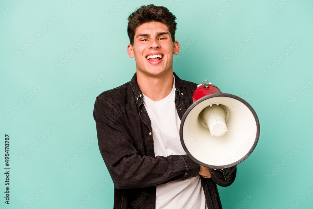 Young caucasian man holding a megaphone isolated on white background laughing and having fun. Young caucasian man holding a megaphone isolated on white background laughing and having fun.