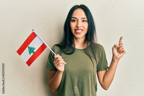 Young hispanic girl holding lebanon flag smiling happy pointing with hand and finger to the side