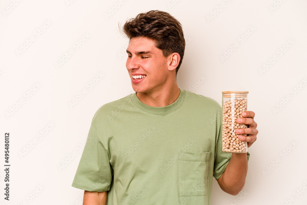 Young caucasian man holding chickpeas isolated on white background looks aside smiling, cheerful and pleasant.