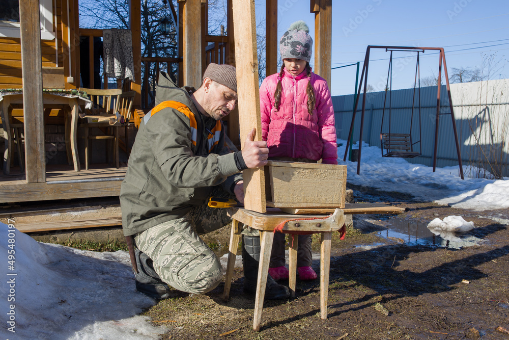 The girl watches her father make a birdhouse with his own hands.