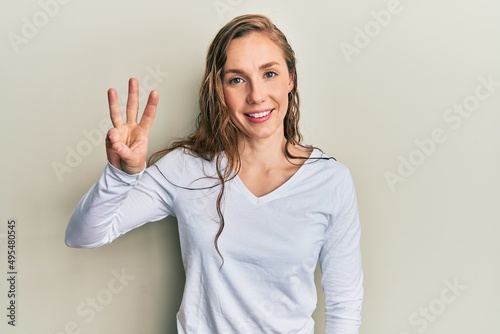 Young blonde woman wearing casual clothes showing and pointing up with fingers number three while smiling confident and happy.