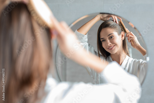 Young Attractive Lady Combing Her Hair With Brush And Looking At Mirror