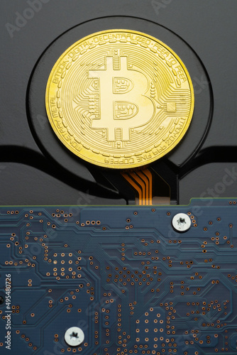 Physical golden Bitcoin criptocurrency coin on hard disk drive with visible printed circuit board and screws