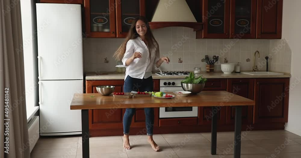Beautiful young woman dancing barefoot in cozy kitchen while cooking vegetarian dinner for family, housewife listen favourite song enjoy healthy lifestyle and food preparation at home. Cookery concept Beautiful young woman dancing barefoot in cozy kitchen while cooking vegetarian dinner for family, housewife listen favourite song enjoy healthy lifestyle and food preparation at home. Cookery concept
