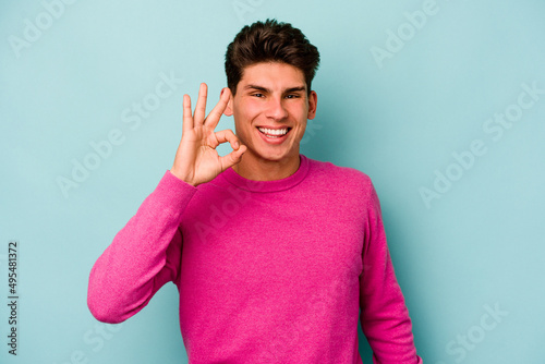 Young caucasian man isolated on blue background cheerful and confident showing ok gesture.