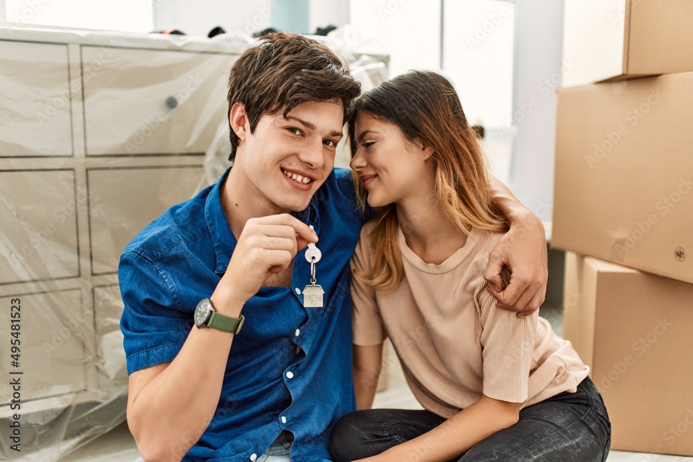 Young caucasian couple smiling happy sitting on the floor holding key of new home. Young caucasian couple smiling happy sitting on the floor holding key of new home.