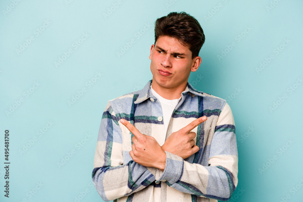 Young caucasian man isolated on blue background points sideways, is trying to choose between two options. Young caucasian man isolated on blue background points sideways, is trying to choose between two options.