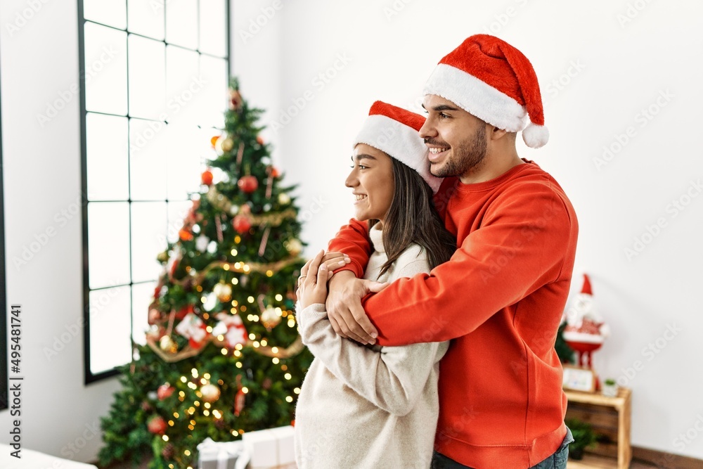 Young hispanic couple standing by christmas tree looking to side, relax profile pose with natural face and confident smile. Young hispanic couple standing by christmas tree looking to side, relax profile pose with natural face and confident smile.
