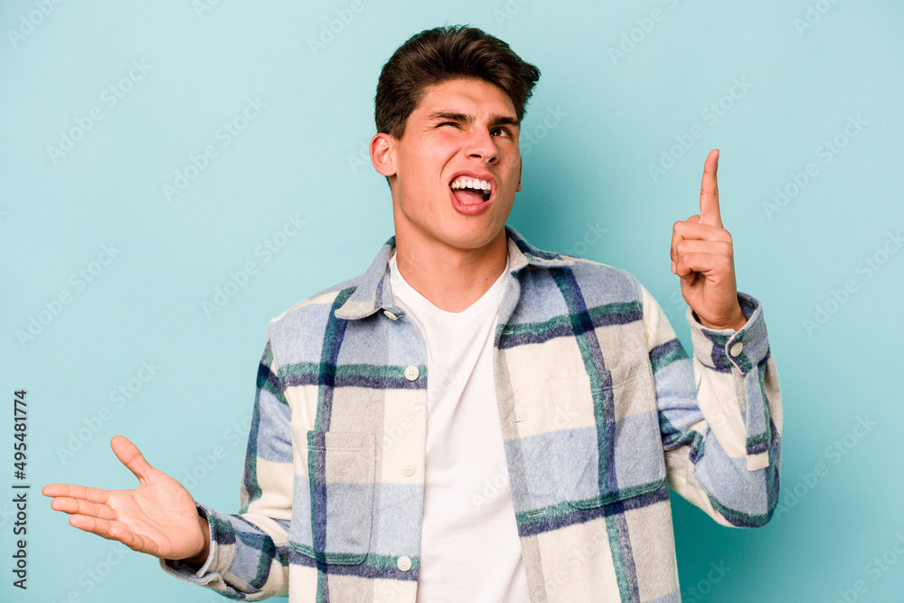 Young caucasian man isolated on blue background holding and showing a product on hand. Young caucasian man isolated on blue background holding and showing a product on hand.