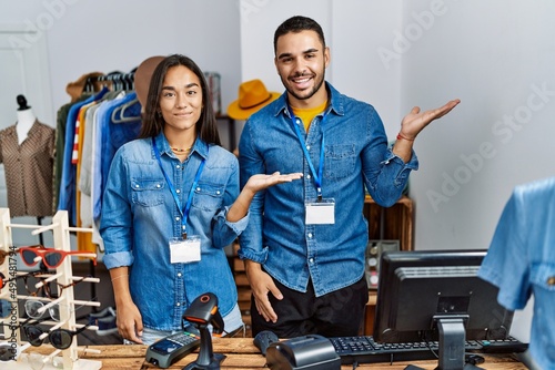 Young interracial people working at retail boutique smiling cheerful presenting and pointing with palm of hand looking at the camera.